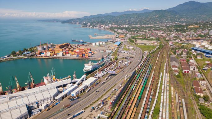 Vue aérienne d'un port avec des conteneurs, des trains et des montagnes en arrière-plan.